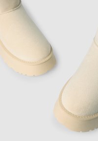 Stivali alla caviglia in suede beige con punta arrotondata e parte superiore testurizzata, dotati di una soletta in gomma beige spessa con dettagli di battistrada pronunciati.