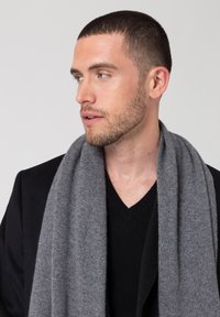 Sciarpa di lana grigia appoggiata su un maglione nero a V, caratterizzata da una texture morbida e un design semplice, indossata da un uomo con i capelli corti.