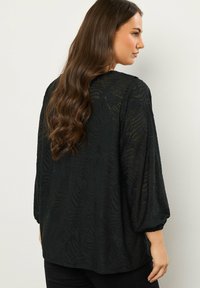Blusa negra con un patrón de cebra texturizado, mangas largas y puños elásticos. La tela ligera cae suelta sobre el cuerpo.