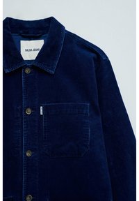 Veste chemise en velours côtelé marine avec un col pointu, des boutons avant, une poche poitrine et un tissu texturé. L'étiquette indique "SALSA JEANS."