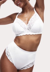 Witte kanten bralette met stippenpatroon en golfrand, gecombineerd met hoge witte slipjes met kanten accenten. Gladde textuur.