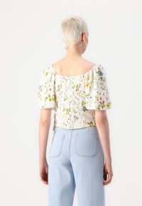 Top floreale bianco con maniche a sbuffo corte e dettaglio arricciato sul retro, abbinato a jeans a gamba larga blu chiaro.