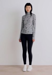 Grau gemustertes Langarmoberteil mit hohem Kragen, schwarze Leggings mit Seitenstreifen, schwarz-weiße Sneaker vor einem neutralen Hintergrund.