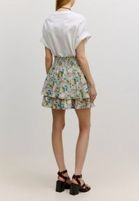 Witte, kortgewaste top gecombineerd met een bloemen, gelaagde mini rok in pastelkleuren. De rok heeft een smock tailleband en meerdere lagen.