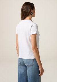 Hvid kortærmet t-shirt med rund halsudskæring og opretstående manchetter, parret med lyseblå brede denim jeans. Glat stoftekstur.