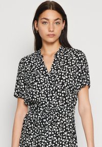 Svart skjortklänning med vitt blommönster, korta ärmar, knäppning fram och midjeband. Lätt och mjukt tyg.