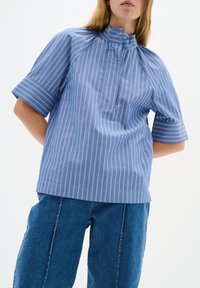 Blå rutig skjorta med hög krage, korta ärmar och bröstficka, tillverkad av ett lätt tyg med en slät textur.