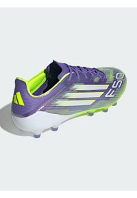 Paarse en gele voetbalschoenen met een gestructureerd oppervlak, slank ontwerp, witte strepen en een doorzichtige plastic zool met zes noppen.