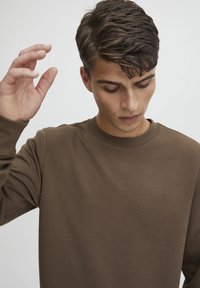 Brun langermet skjorte med rund hals, laget av glatt stoff. Ermene er mansjettert, og passformen virker avslappet og uformell.
