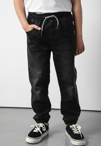 Czarne dżinsowe joggery z elastycznym paskiem w talii, regulowanym sznurkiem, bocznymi kieszeniami i zwężającymi się mankietami, w komplecie z czarnymi trampkami.