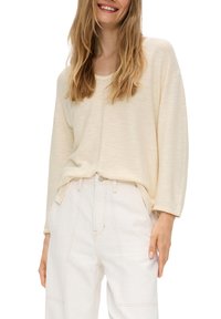 Helles beige Langarmshirt aus strukturiertem Stoff, kombiniert mit hoch taillierten weißen Hosen mit sichtbaren Nahtdetails.
