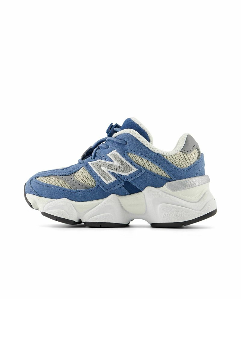 Baskets New Balance bleu et gris avec une épaisse semelle blanche, des panneaux en mesh et un grand logo "N" sur le côté, montrées de l'extérieur.