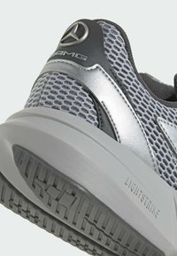 Lehké šedé sportovní boty s síťovaným svrchním materiálem, stříbrnými akcenty a texturovanou gumovou podrážkou označenou "LIGHTSTRIKE." Logo viditelné na boku.