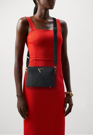 Kobieta w czerwoną sukienkę bez rękawów, nosząca czarną torebkę na ramię ze złotymi akcentami oraz złoto-czerwoną bransoletkę na prawej ręce.