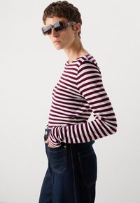 Stripet langermet skjorte i burgunder og hvit, kombinert med mørke denim bukser med høy midje. Tilbehør med store solbriller.