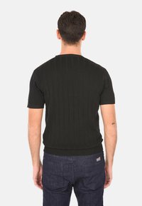 Maglione nero a maniche corte con texture a coste verticali, scollatura rotonda e orlo aderente. Indossato sopra jeans blu scuro.