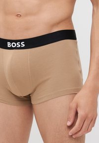 Beige pamut bokszernadrág fekete rugalmas derékpánttal, amelyen a "BOSS" logó fehér betűkkel látható, testhezálló kialakítással és sima textúrával.