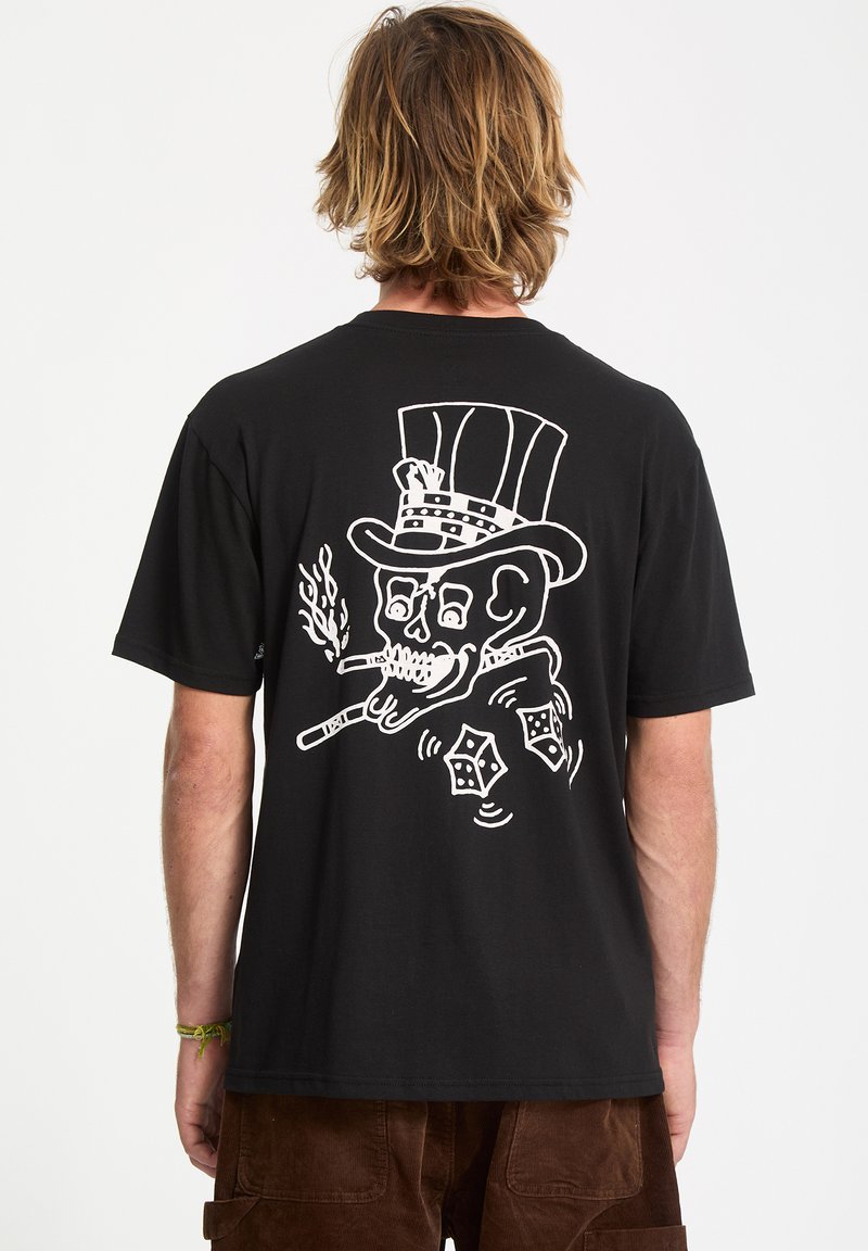 Person with shoulder-length blond hair wearing a black t-shirt featuring a white skull in a top hat smoking cigars with rolling dice design.