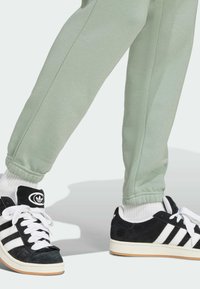Ben har på sig ljusgröna joggers och vita strumpor tillsammans med svarta Adidas-sneakers med vita ränder och gummisulor.