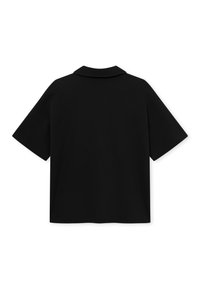 Fekete, rövid ujjú pólóing lapos gallérral, hátulról látható fehér háttér előtt.