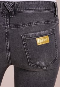 Jeans de mezclilla gris oscuro por detrás con una etiqueta de marca rectangular dorada en el bolsillo derecho y sutiles detalles desgastados.