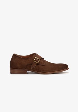 Brown suede shoe with a rounded toe, single strap and brass buckle detail. Flat wooden heel, smooth texture, and stylish minimal design.