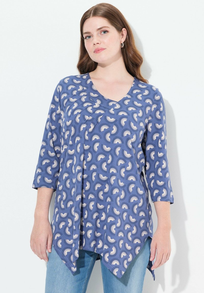 Pullover-Oberteil mit V-Ausschnitt, ¾-Ärmeln und asymmetrischem Saum, aus einem blauen Stoff mit einem cremefarbenen abstrakten Muster. Weicher Stoff.