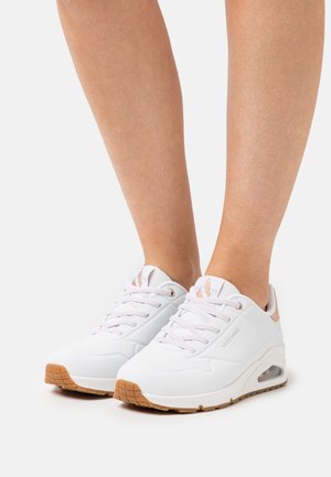 Weiße Sportschuhe mit einer strukturierten Oberseite, Schnürdesign, Gumminochensohle und sichtbarer Luftpolsterung an der Ferse.