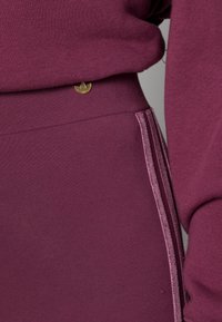 Maroon athletic sweatshirt and leggings set. Features soft fabric, ribbed cuffs, and gold logo accent on waistband. Textured vertical stripe detail.