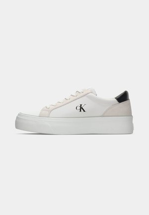 White sneaker with a grey suede accent and black heel. Features a thick white sole and a stitched logo "cK" on the side. Classic lace-up design.