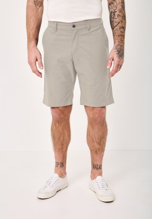Man wearing light gray knee-length shorts, white sneakers, and visible tattoos on forearms and lower legs.