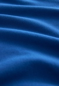 Modrá látka s jemnou textúrou, ktorá zobrazuje jemné vlny a sklady vytvárajúce mäkké tiene a svetlá.