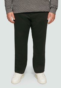 Dunkelgrüne Hose aus glattem Stoff, mit geradem Schnitt, kombiniert mit weißen Sneakers. Keine auffälligen Muster oder Beschläge sichtbar.
