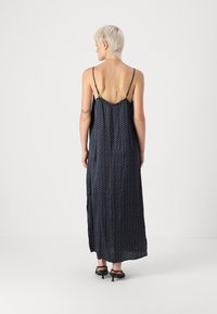 Navy blue sleeveless maxi dress with white polka dots, featuring a low back and side slits, made of lightweight fabric. Worn with black heels.