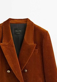 Blazer en velours côtelé marron avec un design croisé à double boutonnage, des revers crantés et des boutons dorés. Comprend une poche poitrine et une doublure noire.