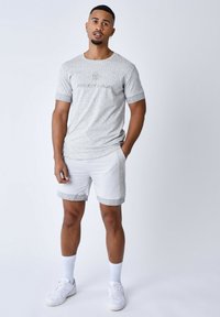 T-shirt gris à motifs avec le logo "Project Paris", associé à un short blanc comportant un motif similaire sur les côtés et des bordures grises. Baskets blanches.