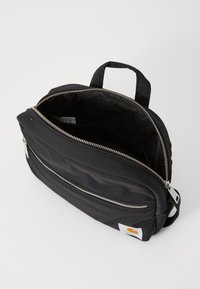 Zaino in tessuto nero con maniglia superiore e zip argento. Presenta un compartimento principale e una tasca esterna con zip. Patch con logo dettagliato.