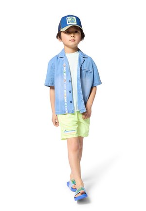 Denim overhemd met korte mouwen, lichtblauw, met kleurrijke tekst; mintgroene korte broek; blauwe plastic sandalen met een accent. Hoed met logo, donkerblauw.