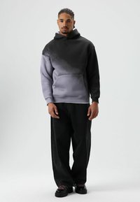 Zwart-grijze hoodie met een kangoeroezak, geribbelde manchetten en een losse pasvorm, gecombineerd met losse zwarte jeans en zwarte schoenen.