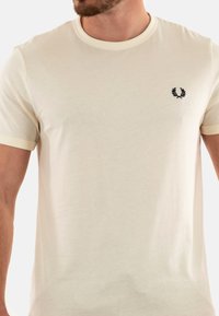 T-shirt beige a col rotondo realizzato in morbido tessuto, con un piccolo logo ricamato scuro sul lato sinistro del petto e polsini a coste in contrasto.