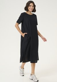 Schwarzes knielanges Kleid mit kurzen Ärmeln, Seitentaschen und lockerer Passform. Hergestellt aus einem leichten Stoff, mit einem runden Ausschnitt.