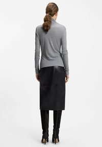 Grijs langmouwen coltrui gecombineerd met een zwarte leren midi-rok, die een gladde textuur en een getailleerde Silhouette heeft. Zwarte kniehoge laarzen maken de look af.