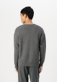 Grijze gebreide trui met een ronde hals, ontspannen pasvorm en geribde boord. Textuurstof met een subtiel patroon, gedragen met grijze gestreepte broek.