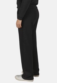Pantalones de chándal negros con un corte relajado, confeccionados en material suave, con una cintura elástica y bolsillos laterales, combinados con zapatillas blancas.