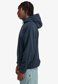 Marineblå fleece hoodie med en frontlomme, justerbar snørrehette og sidelukning. Struktureret overflade med en afslappet pasform.