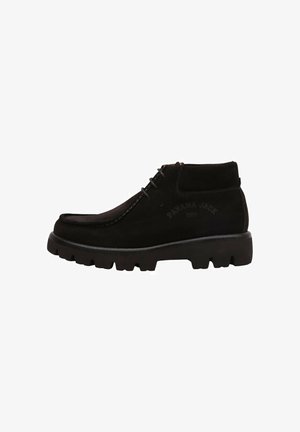 Botas negras de ante hasta el tobillo con una suela de goma resistente, que cuentan con una puntera de estilo mocasín y un sutil logo en el lateral. Diseño de cierre con cordones.
