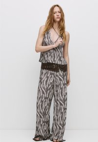 Grijze en witte gestreepte haltertop en wijde broek combinatie met een bruine gesp met studs. Lichtgewicht stof met een vloeiende textuur.
