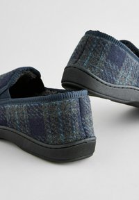 Blå og grå ternede slippers lavet af tekstureret filt med en sort gummisål og polstret krave, der har et enkelt, lavprofil design.