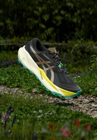 Chaussure de course noire avec une tige en mesh texturé, des accents jaunes et turquoise, et une semelle intermédiaire blanche épaisse, dotée d'une semelle extérieure à motif pour une meilleure adhérence.