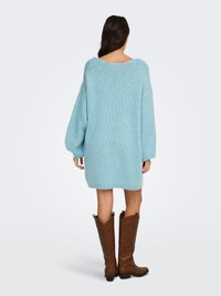 Light blue knitted oversized sweater dress with a wide neckline and long sleeves, paired with brown leather cowboy boots.